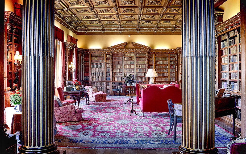 Highclere Castle library with ornate ceiling, bookshelves, and red furnishings.