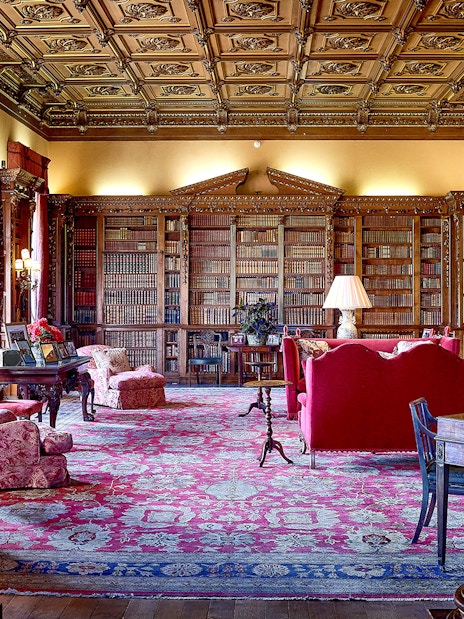 Highclere Castle library with ornate ceiling, bookshelves, and red furnishings.