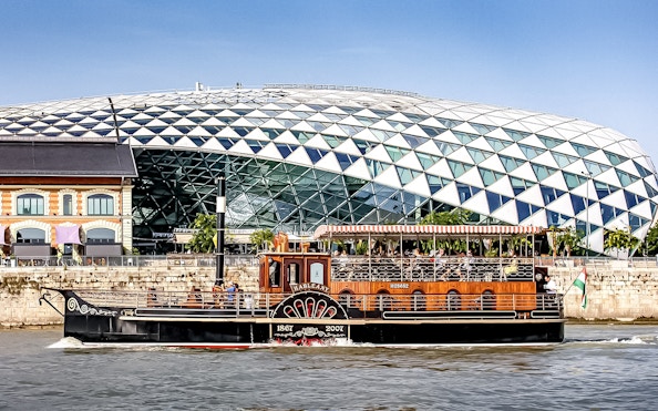 Cruise boat on the Danube River in Budapest with modern glass building in background.