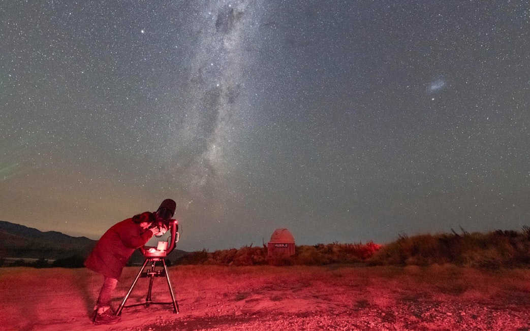 Person setting up a telescope under a starry sky at The Crater Stargazing Experience.