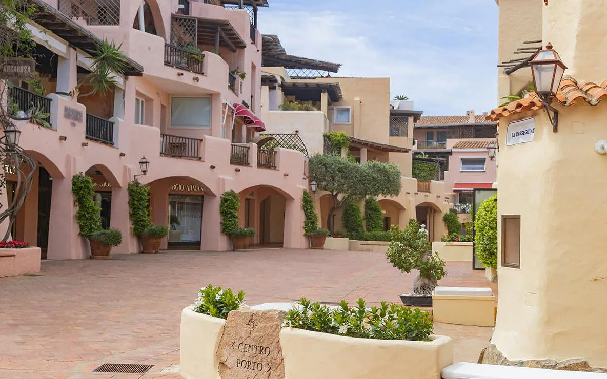 Porto Cervo town square with pastel buildings and greenery, Alghero guided tour.