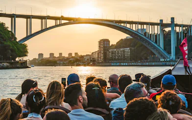 Tourists on a boat ride enjoying sunset view under a bridge in Porto, Portugal.
