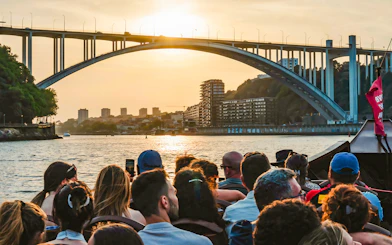 Tourists on a boat ride enjoying sunset view under a bridge in Porto, Portugal.
