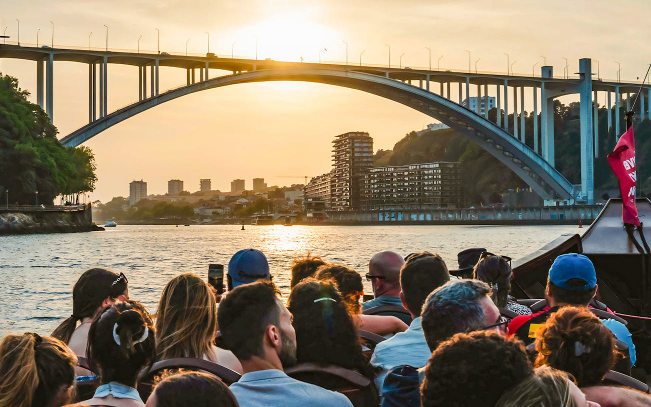 Tourists on a boat ride enjoying sunset view under a bridge in Porto, Portugal.