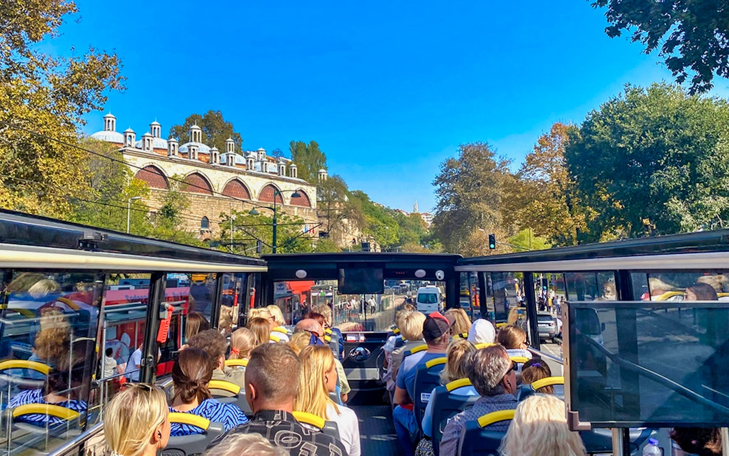 Open-top bus tour with passengers viewing Istanbul's historic architecture along the Bosphorus.