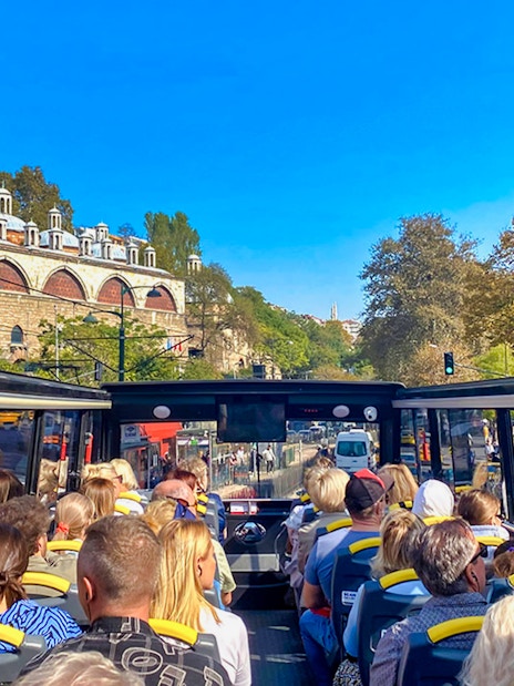 Open-top bus tour with passengers viewing Istanbul's historic architecture along the Bosphorus.