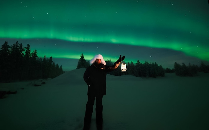 Person holding lantern under Northern Lights on Discovery Tour.