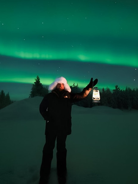 Person holding lantern under Northern Lights on Discovery Tour.