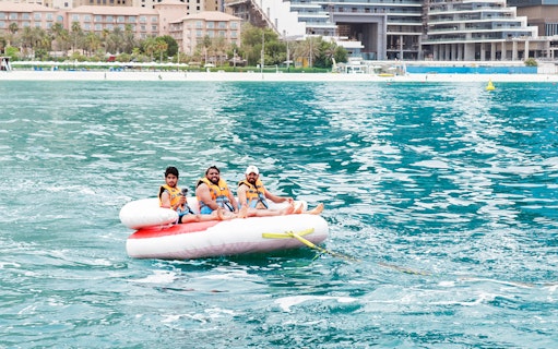 Three people enjoying a donut ride on the water near a beach resort.