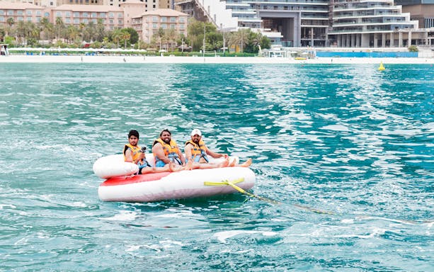 Three people enjoying a donut ride on the water near a beach resort.