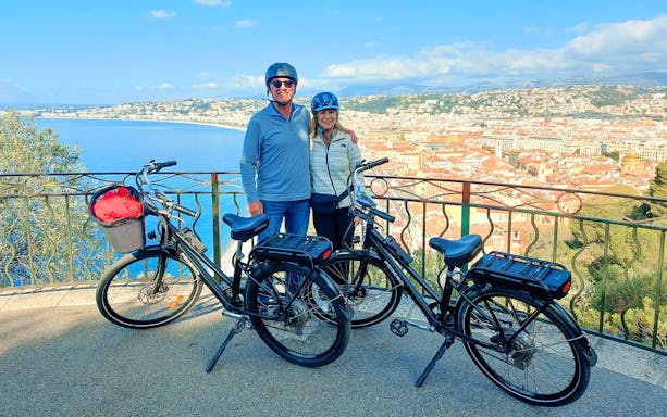 Couple with e-bikes overlooking the French Riviera coastline.