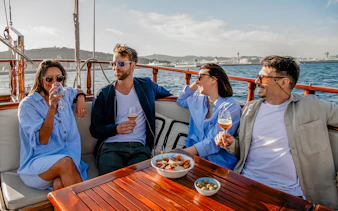 Group enjoying drinks on a catamaran in Barcelona with cityscape in the background.