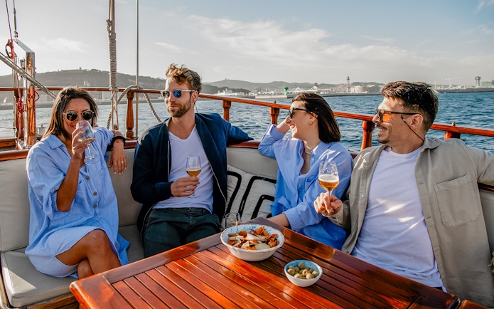 Group enjoying drinks on a catamaran in Barcelona with cityscape in the background.