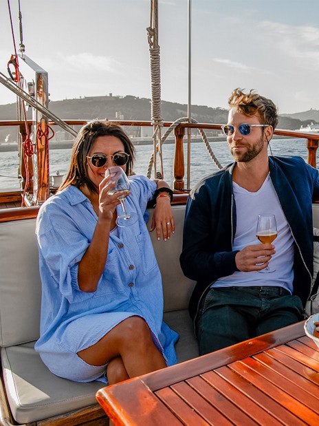 Group enjoying drinks on a catamaran in Barcelona with cityscape in the background.