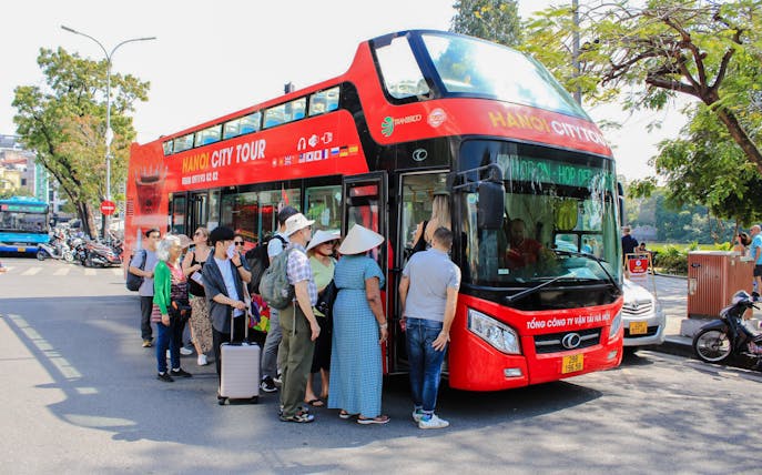 Tourists boarding a red hop-on hop-off bus in Hanoi, Vietnam.