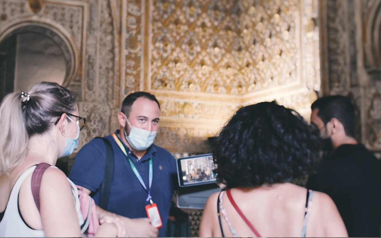 Visitors on a guided tour inside the Alcázar, observing intricate wall details.