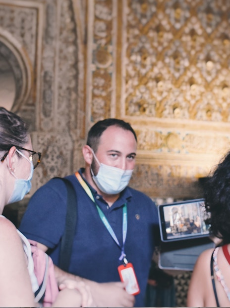 Visitors on a guided tour inside the Alcázar, observing intricate wall details.