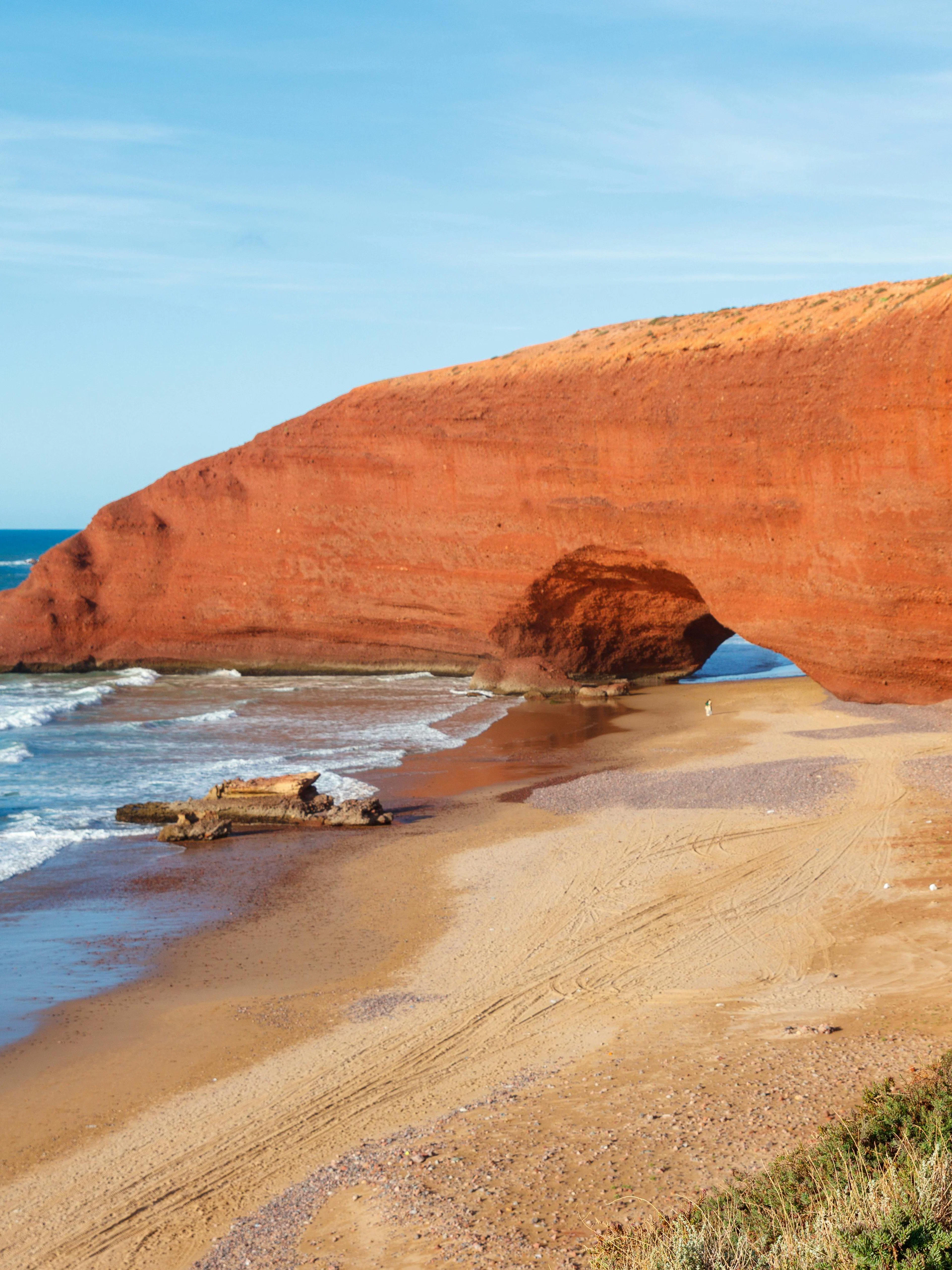 Woman sitting and viewing red rock arches at Legzira Beach, Morocco.