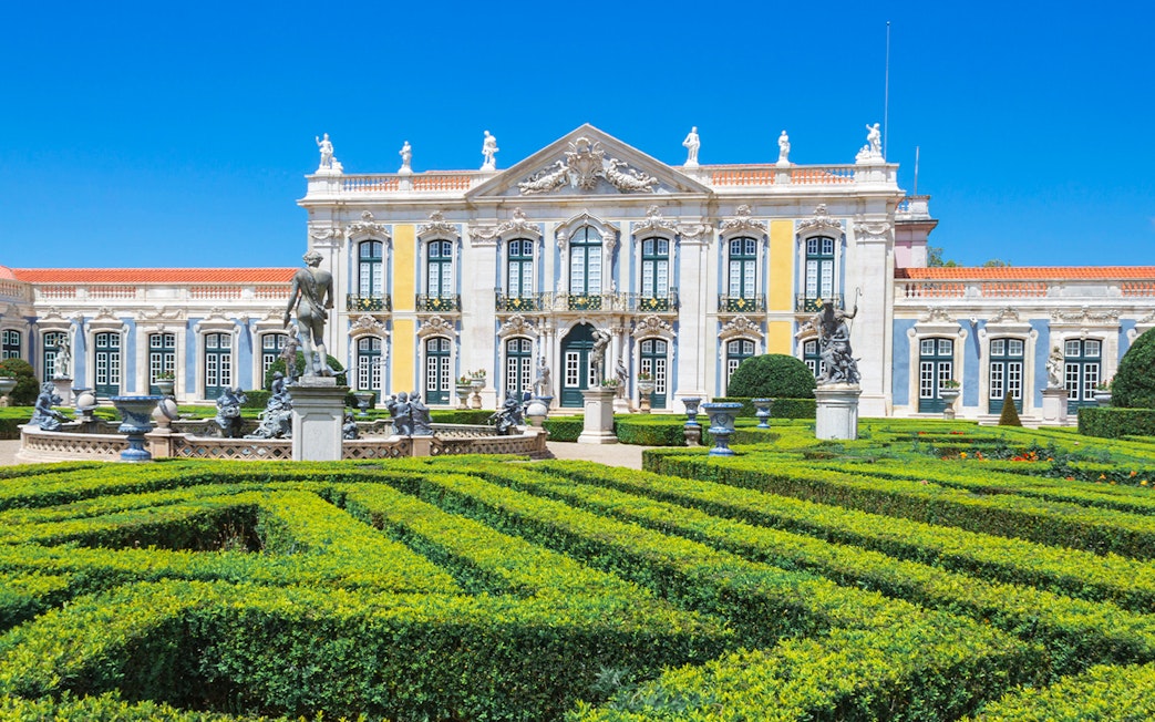 Queluz National Palace facade with manicured gardens and statues, Portugal.