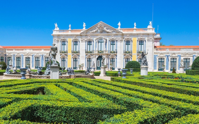 Queluz National Palace facade with manicured gardens and statues, Portugal.