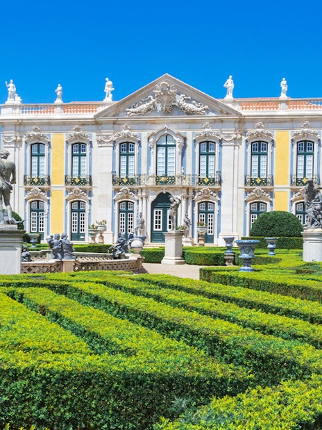 Queluz National Palace facade with manicured gardens and statues, Portugal.
