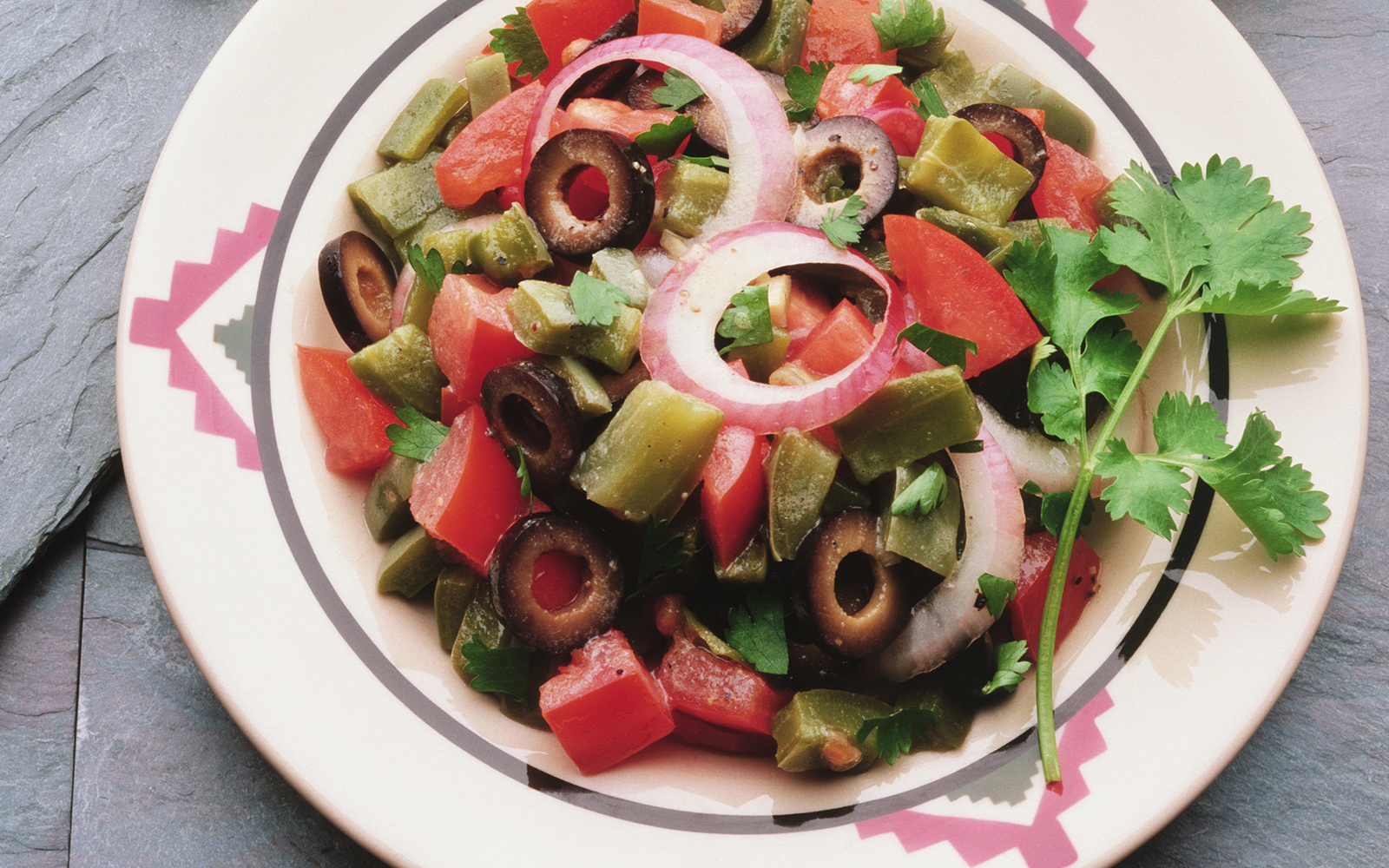 Mexican salad with tomatoes, olives, onions, and cilantro on a decorative plate.