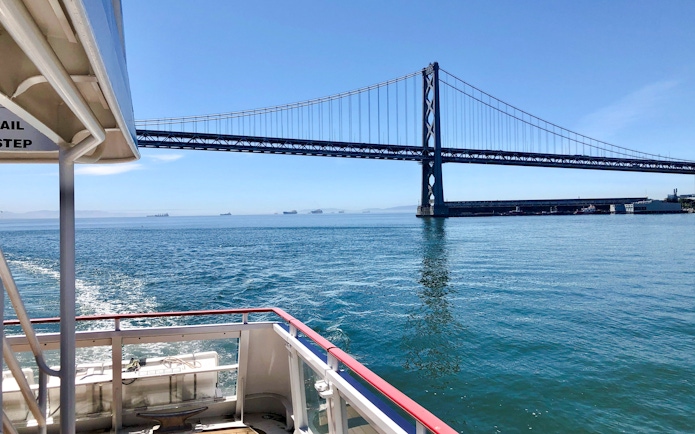 Cruise boat approaching San Francisco Bay Bridge on a sunny day.