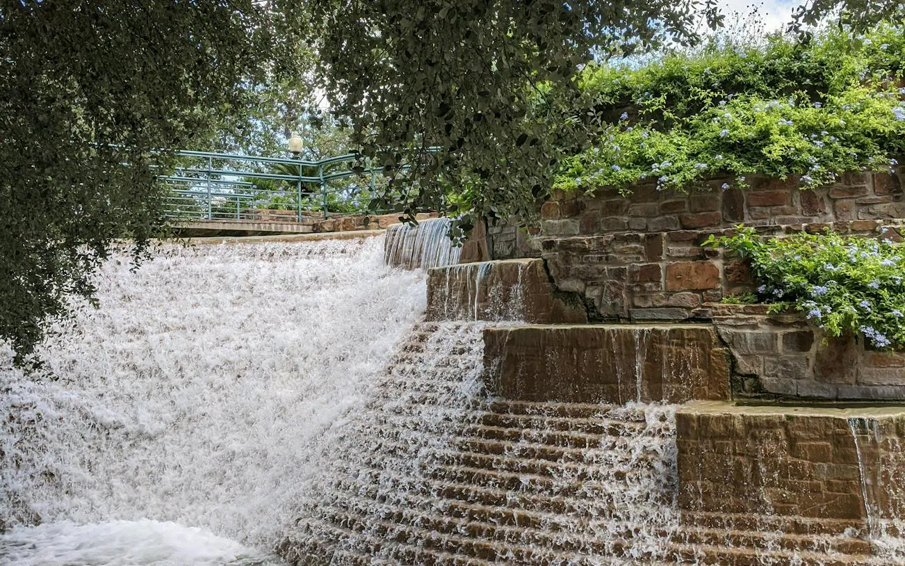 Waterfall cascading over stone steps in a lush garden, San Antonio exploration game.