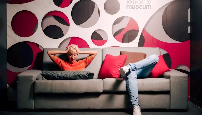 Person sitting on a sofa in the Paradox Sofa room at Paradox Museum Paris with a geometric wall design.
