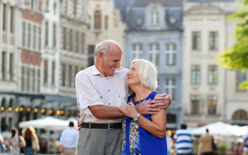 Elderly couple embracing in Bruges city square during day trip from Brussels.