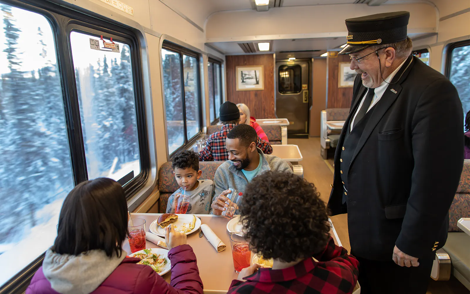 Guests dining on the Aurora Winter Train, Alaska Railroad, with snowy landscape views.