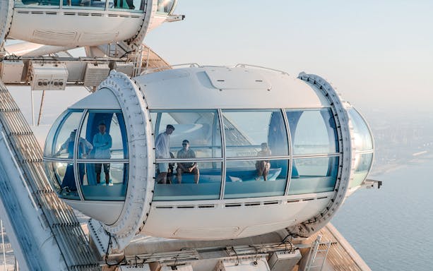 Ain Dubai observation pod with people enjoying views of the city and sea.