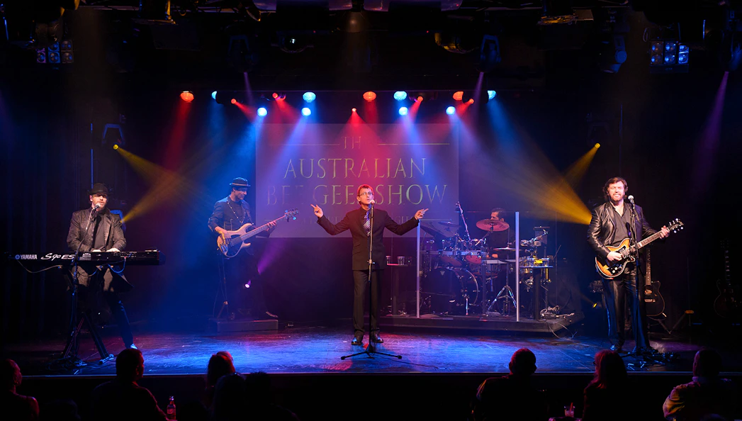 Performers on stage during The Australian Bee Gees Show with colorful lights.