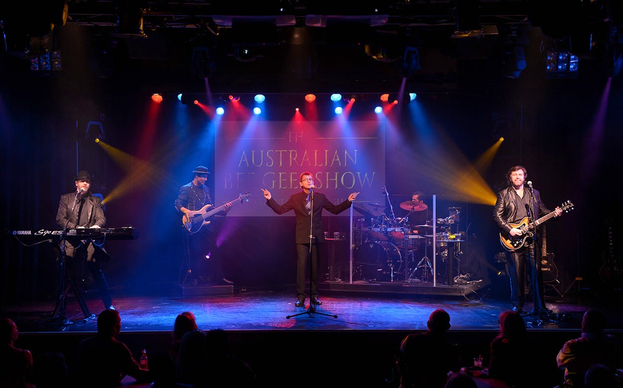 Performers on stage during The Australian Bee Gees Show with colorful lights.