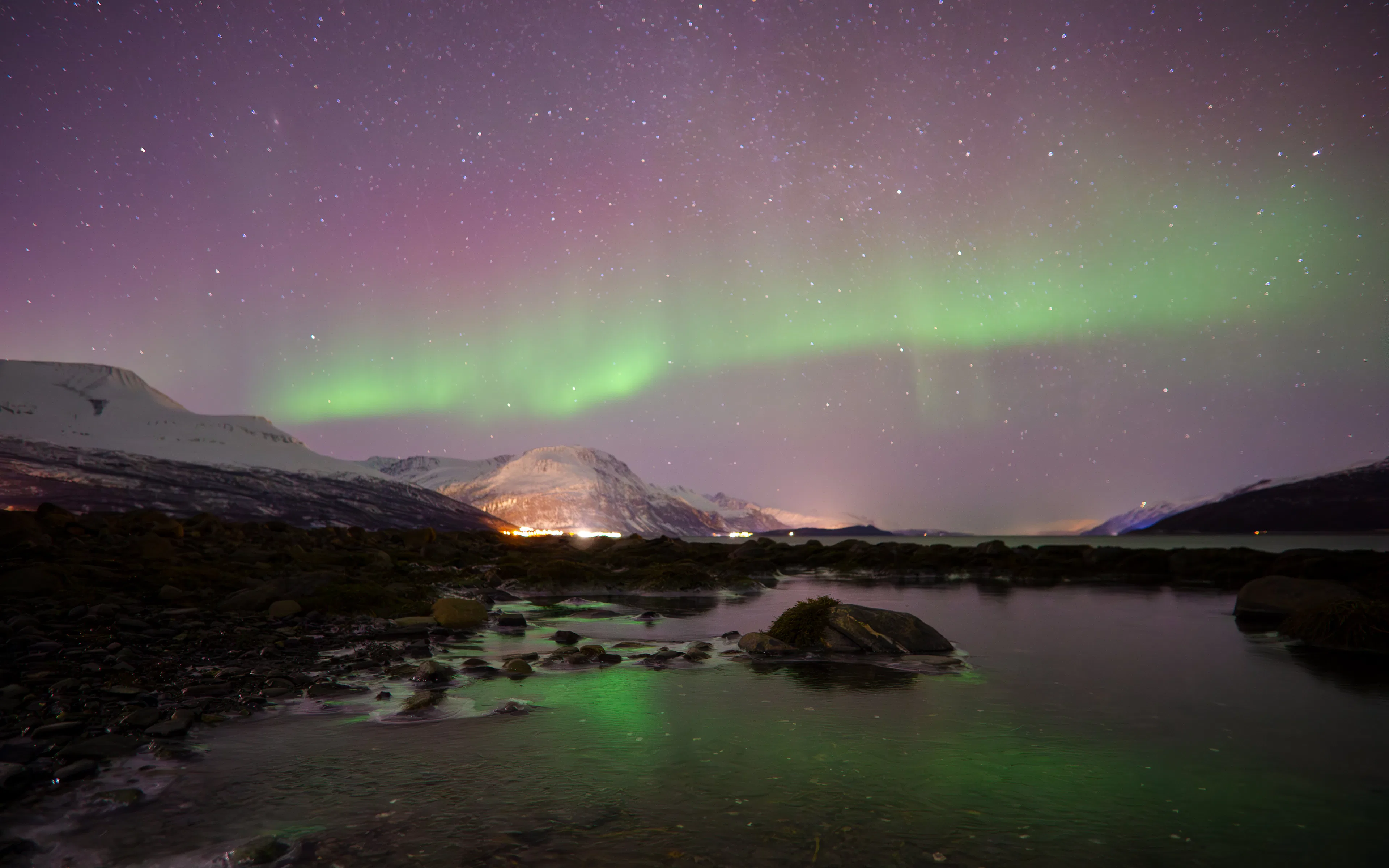 Aurora borealis over snowy mountains and water in Skibotn, Norway.