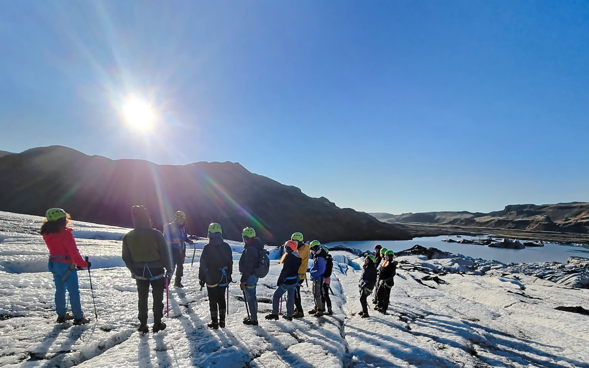 Tourists exploring Sólheimajökull glacier near Reykjavik under a clear sky.
