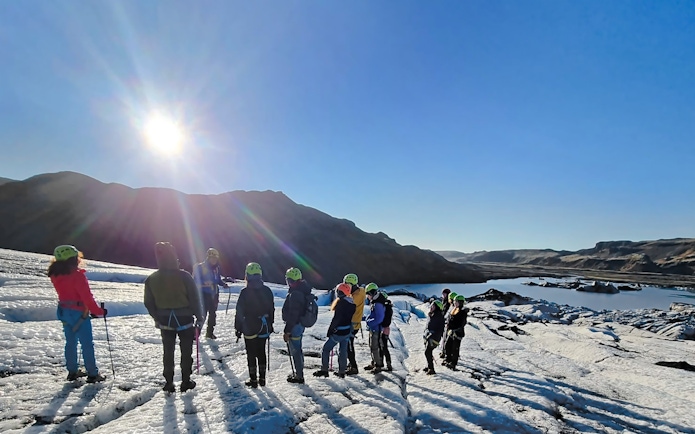 Tourists exploring Sólheimajökull glacier near Reykjavik under a clear sky.