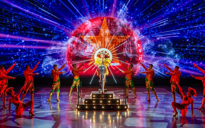 Performers in vibrant costumes on stage with colorful lights at a Colosseum show.
