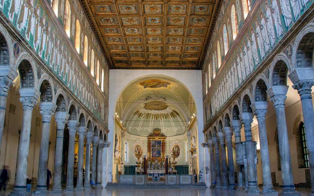 Interior of Basilica di Sant'Apollinare Nuovo in Ravenna, showcasing detailed mosaics and columns.