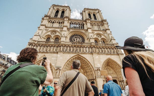 Tourists viewing Notre Dame Cathedral facade in Paris, France.