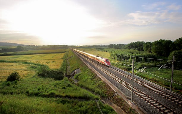 High-speed train traveling through Italian countryside at sunrise.