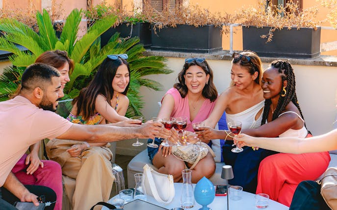 Friends toasting with drinks on a rooftop in Rome.