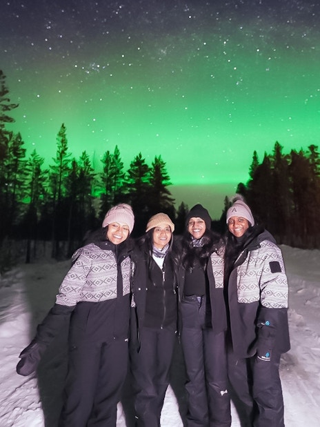 Small group viewing Northern Lights in snowy forest, Levi.