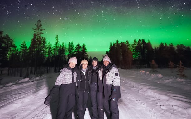 Small group viewing Northern Lights in snowy forest, Levi.