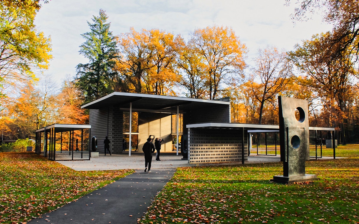 Kröller-Müller Museum entrance with sculpture, surrounded by autumn trees in Hoge Veluwe National Park.
