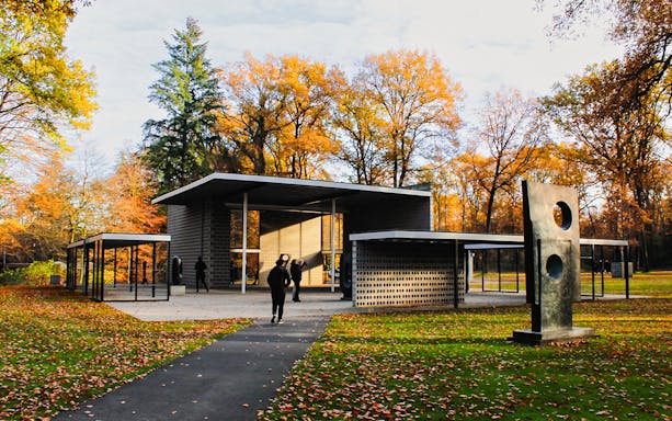 Kröller-Müller Museum entrance with sculpture, surrounded by autumn trees in Hoge Veluwe National Park.