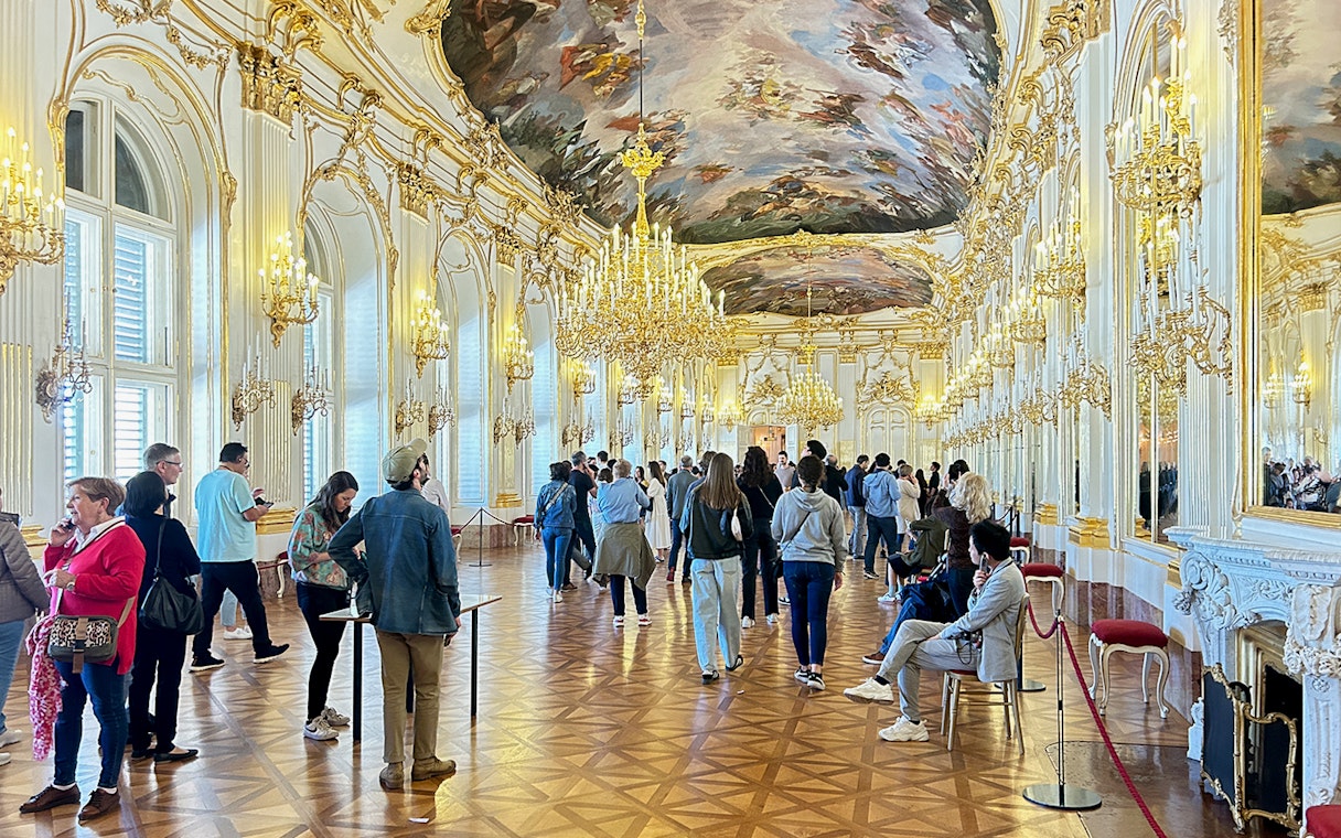 Visitors exploring the opulent hall with chandeliers inside Schönbrunn Palace, Vienna.