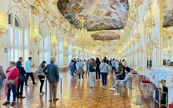 Visitors exploring the opulent hall with chandeliers inside Schönbrunn Palace, Vienna.