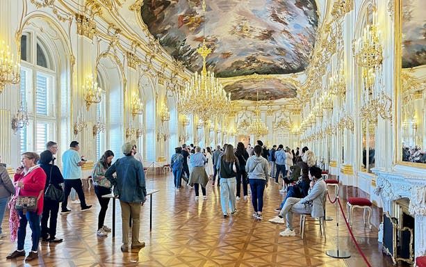 Visitors exploring the opulent hall with chandeliers inside Schönbrunn Palace, Vienna.