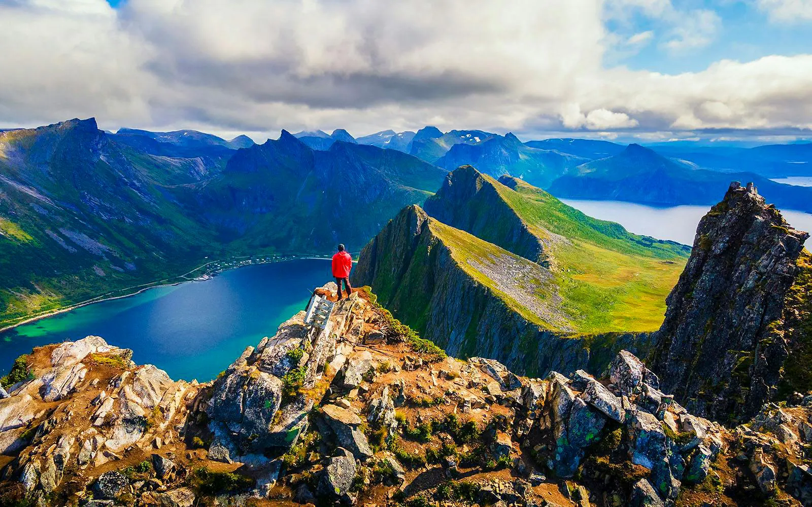 Person standing on rocky peak overlooking Arctic fjord landscape, Tromso expedition.